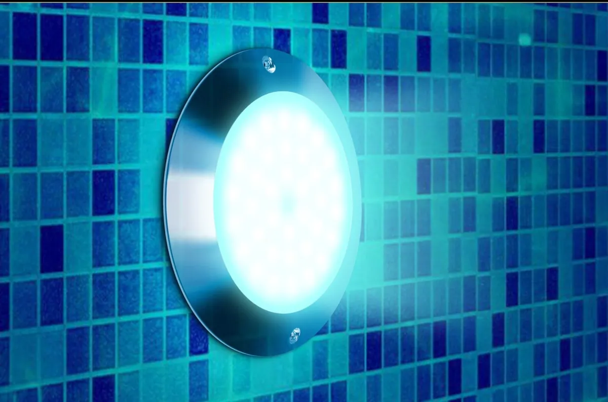 A round pool light glowing on a blue mosaic pool wall
